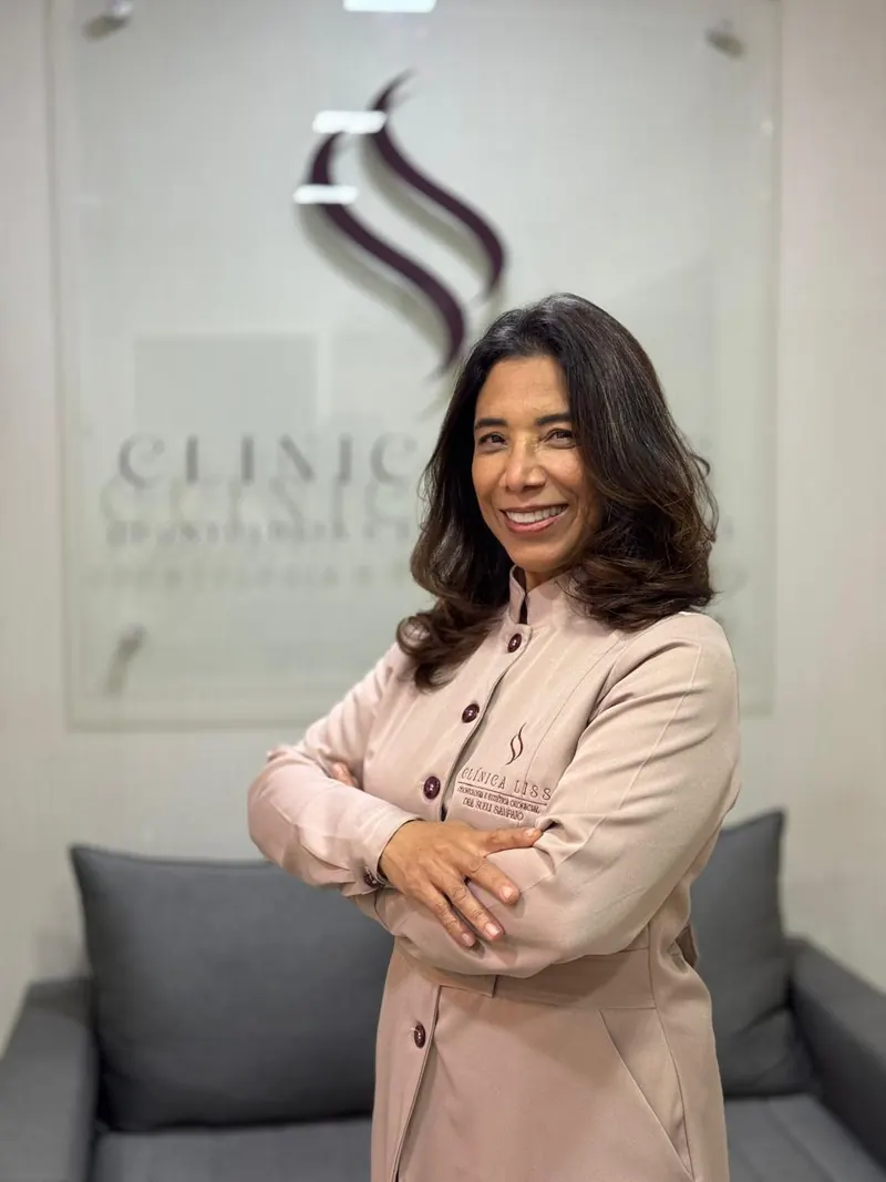 Dra. Sueli Sampaio na Clínica Liss, diante da parede com a marca da clínica